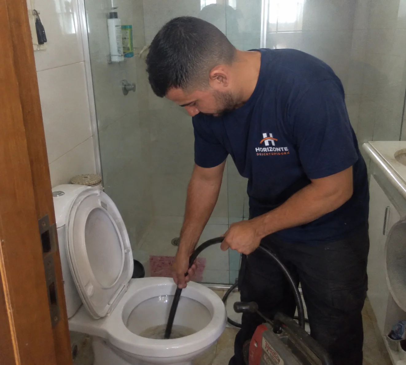 Técnico da Horizonte desentupindo um vaso sanitário com equipamento profissional.